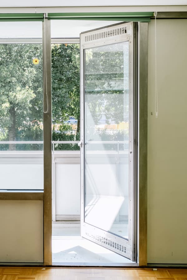 Architectural project - balcony, airy interior, open door, green view, light wood floor, fresh atmosphere, minimalist, wood, metal frame, city living, metal, natural light, sustainable design, glass, contemporary style, green, daylight, beige, eco friendly, modern design, simple design, clean lines, white walls, indoor outdoor, white, large window, cozy corner, residential space, glass door, home design, seamless transition, glass facade, sliding door, connection to nature, calming vibe, spacious feel, bright room, urban apartment