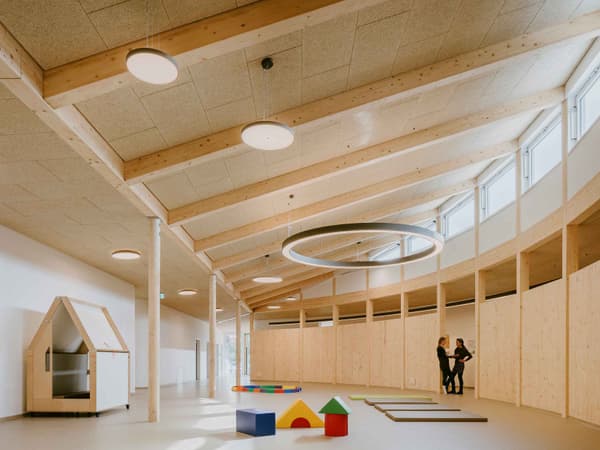Architectural project - open ceiling, muted colors, playful area, cream, acoustic panels, soft lighting, wood, timber, warm tones, eco design, neutral tones, timber structure, exposed beams, beige, Scandinavian style, neutral palette, minimalist design, gathering area, community center, creative space, light tones, sustainable building, Nordic design, open plan, inviting space, wooden architecture, child friendly, wooden flooring, bright interior, educational space, modern interior, play area, family-friendly, versatile space