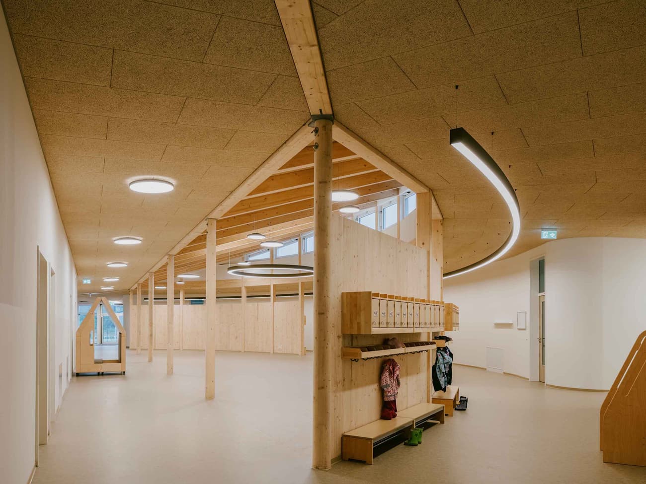 Architectural project - ceiling lights, curved ceiling, communal area, modern space, multifunctional hall, natural materials, wood, timber, natural light, sustainable design, warm tones, green building, neutral tones, timber structure, exposed beams, daylight, plywood, beige, light wood, natural wood, eco friendly, honey wood, wood beams, organic design, Scandinavian style, neutral palette, public space, gathering area, community center, social hub, timber walls, circular design, clean lines, wood cladding, Nordic design, beige tones, open layout, bright interior, wood ceiling, educational space, kid friendly, warm lighting, learning environment, welcoming space, minimalist interior, family-friendly, wooden walls