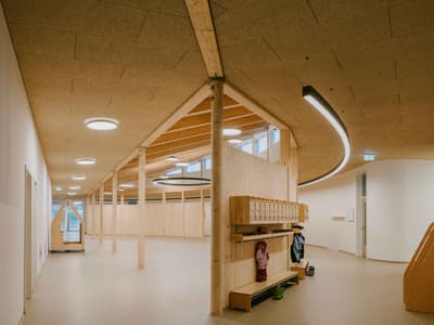Architectural project - ceiling lights, curved ceiling, communal area, modern space, multifunctional hall, natural materials, wood, timber, natural light, sustainable design, warm tones, green building, neutral tones, timber structure, exposed beams, daylight, plywood, beige, light wood, natural wood, eco friendly, honey wood, wood beams, organic design, Scandinavian style, neutral palette, public space, gathering area, community center, social hub, timber walls, circular design, clean lines, wood cladding, Nordic design, beige tones, open layout, bright interior, wood ceiling, educational space, kid friendly, warm lighting, learning environment, welcoming space, minimalist interior, family-friendly, wooden walls