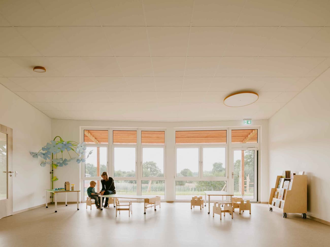 Architectural project - sustainable space, indoor play, wooden toys, airy room, inviting, spacious, educational environment, warm interior, natural materials, eco-friendly design, wood, natural light, community space, neutral tones, daylight, beige, light wood, Scandinavian style, neutral palette, minimalist design, social space, interactive space, multifunctional, creative space, large windows, white, Nordic design, cozy vibe, open layout, family space, child friendly, bright interior, calm atmosphere, simple decor, open space, educational space, playroom, learning environment, family area