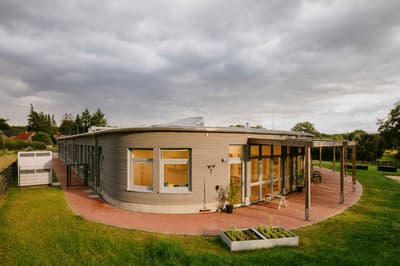 Architectural project - floor to ceiling windows, pergola, patio space, terracotta tiles, horizontal cladding, suburban setting, wood, metal, outdoor space, natural light, sustainable design, glass, warm tones, eco design, contemporary architecture, grey, neutral tones, timber structure, daylight, beige, brown, concrete, flat roof, rustic vibe, minimalist design, glass doors, low carbon, passive house, modern facade, wood cladding, white, inviting home, energy efficient, compact design, green home, terracotta, garden view, nature integration, cozy exterior, residential home, family house