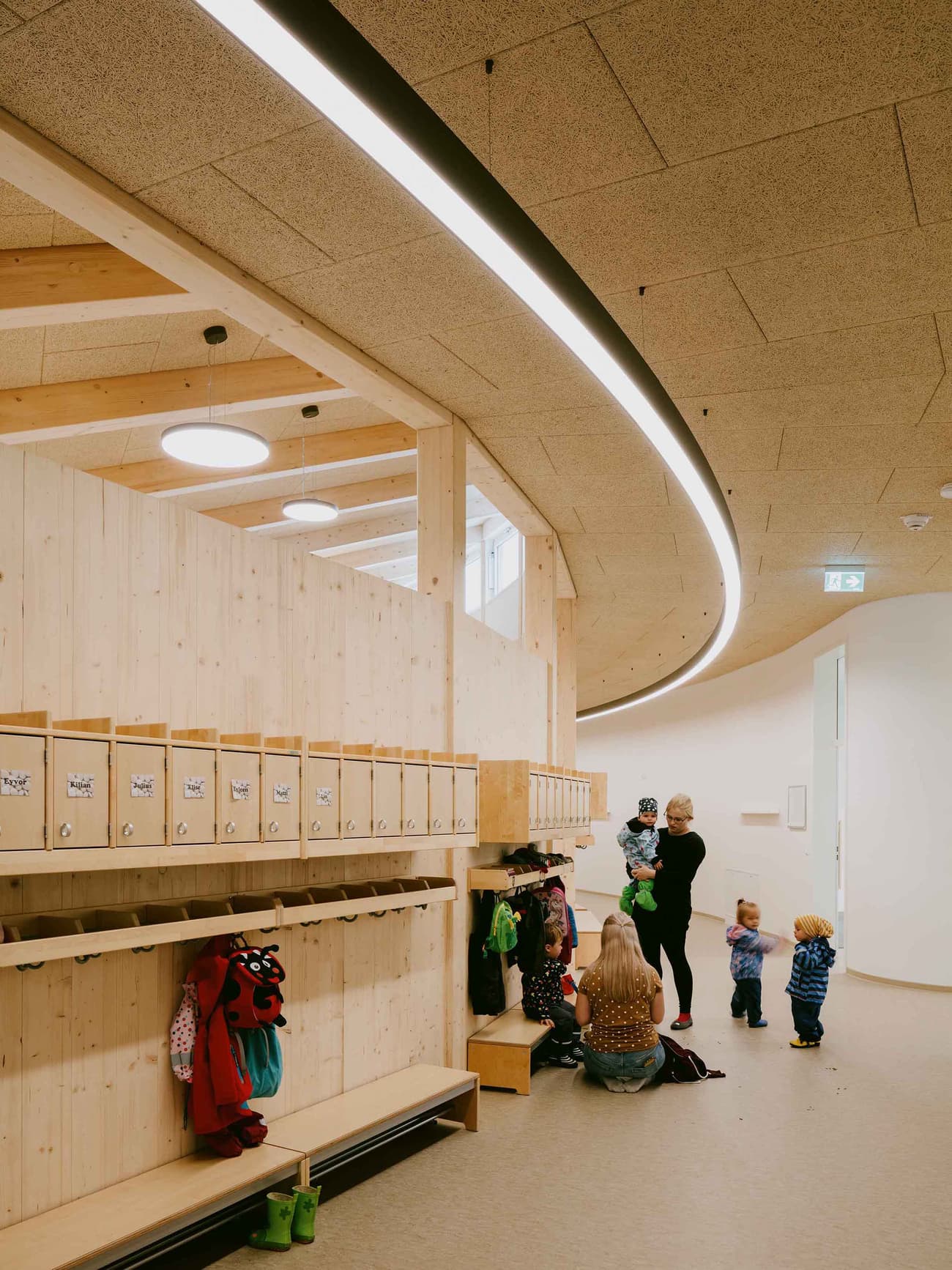 Architectural project - flexible space, overhead lighting, textured ceiling, curved ceiling, recessed lighting, indoor environment, minimal design, warm interior, natural materials, wood, timber, inviting atmosphere, sustainable design, warm tones, green building, community space, gathering space, beige, light wood, natural wood, eco friendly, honey wood, contemporary design, Scandinavian style, social space, interactive design, light tones, timber walls, biophilic design, white, Nordic design, cozy vibe, wooden interior, wood walls, open plan, child friendly, educational space, playful space, simple lines, learning environment, welcoming space, family-friendly