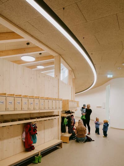 Architectural project - flexible space, overhead lighting, textured ceiling, curved ceiling, recessed lighting, indoor environment, minimal design, warm interior, natural materials, wood, timber, inviting atmosphere, sustainable design, warm tones, green building, community space, gathering space, beige, light wood, natural wood, eco friendly, honey wood, contemporary design, Scandinavian style, social space, interactive design, light tones, timber walls, biophilic design, white, Nordic design, cozy vibe, wooden interior, wood walls, open plan, child friendly, educational space, playful space, simple lines, learning environment, welcoming space, family-friendly
