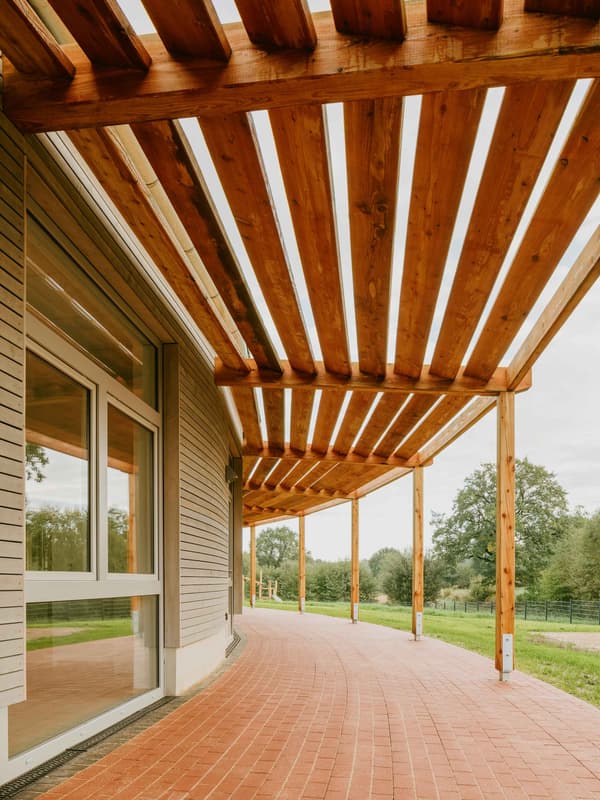 Architectural project - garden architecture, shade structure, open sky, garden patio, wooden pergola, timber pergola, curved path, lush landscape, red bricks, timber slats, brick path, pergola design, relaxation space, natural materials, wood, timber, raw materials, outdoor space, natural light, inviting atmosphere, outdoor living, passive design, sustainable design, warm tones, beige, brown, exterior design, daylight optimization, eco friendly, window view, earthy tones, garden feature, terracotta, brick, landscape design, greenery, wooden deck, outdoor retreat, natural surroundings, red