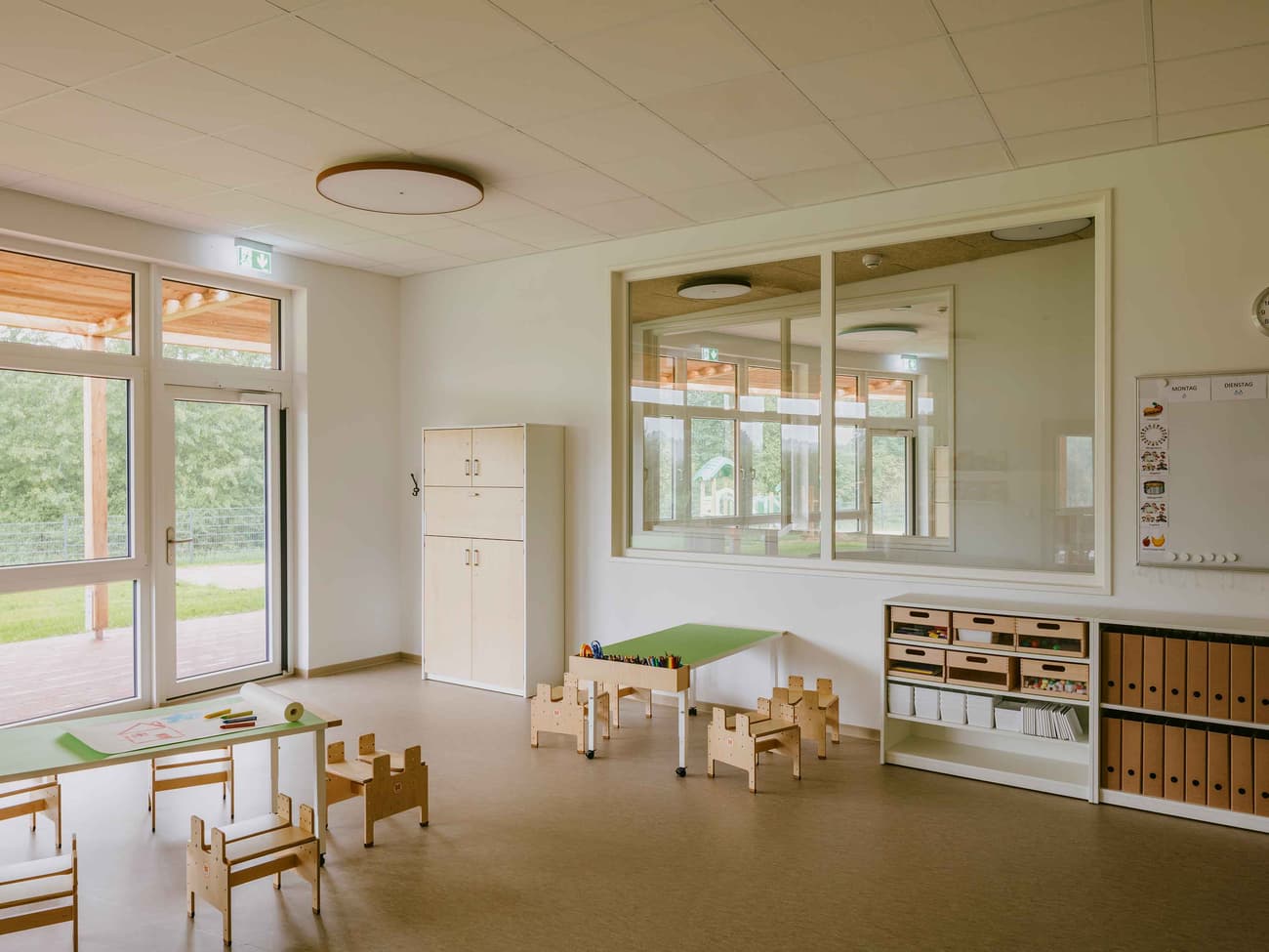 Architectural project - glass partition, beige floor, spacious room, educational environment, creativity space, natural materials, eco-friendly design, natural light, inviting atmosphere, warm tones, honey wood, contemporary design, neutral palette, minimalist design, cozy space, clean lines, white walls, large windows, indoor outdoor connection, child friendly, bright interior, functional layout, simple decor, educational space, playroom, sustainable interior, learning environment, calm setting, play area