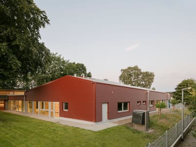 Architectural project - metal cladding, metallic finish, metal facade, bright red, green environment, red facade, red building, easy access, educational facility, grass lawn, sustainable materials, steel, metal, outdoor space, natural light, passive design, eco-conscious, sustainable design, glass, green building, community space, contemporary architecture, grey, green, neutral tones, daylight, exterior design, functional design, eco friendly, simple design, community hub, low carbon, biophilic design, landscape integration, clean lines, large windows, minimal aesthetic, energy efficient, rural setting, open space, modern exterior, school building, public building, glass facade, modern school, green roof potential, nature setting, red