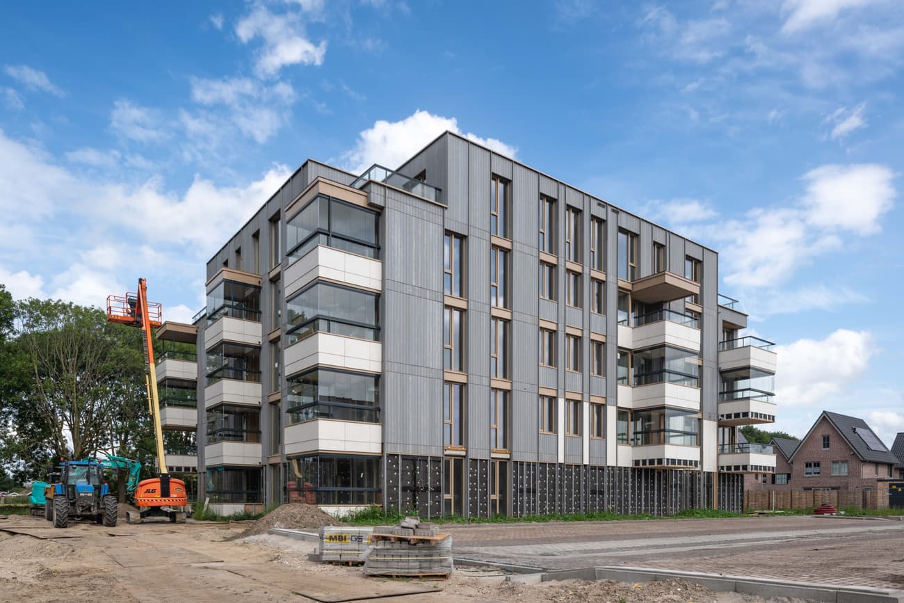 Architectural project - multi-story building, angular design, cubic form, metal accents, circular economy, community living, facade cladding, steel frames, minimal design, modular construction, outdoor area, grey, construction site, urban development, engineered wood, glass panels, flat roof, contemporary design, light tones, sustainable building, machinery, passive house, natural ventilation, modern facade, clean lines, large windows, timber cladding, white, modern architecture, concrete base, eco-friendly structure, exterior view, residential building, floor to ceiling glass, vertical panels, energy efficiency, urban housing