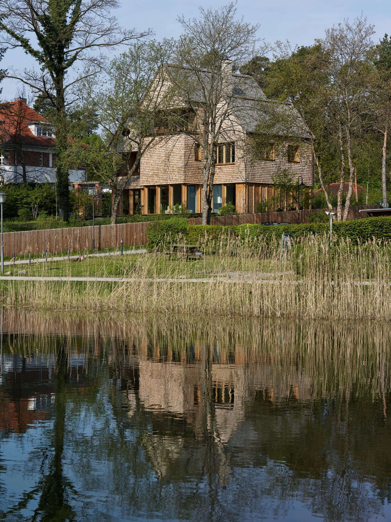 Architectural project - wood, timber, sustainable design, warm tones, green, neutral tones, beige, brown, timber facade, natural setting, neutral colors, passive house, wood cladding, rural home, energy efficient, green home, earthy tones, wooden shingles, pitched roof, nature-inspired, organic materials, environmental design, tranquil environment, biophilic architecture, woodland retreat, eco cabin, lake house, waterfront home, rustic retreat, forest house, serene escape, glass windows, reflective surface, lakeside view, outdoor harmony, vertical siding, cozy exterior, landscape blending, scenic architecture, countryside living, natural habitat, traditional touch, integrated design, eco architecture