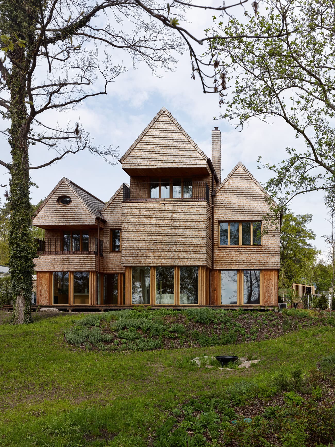 Architectural project - wood, timber, raw materials, natural light, outdoor living, glass, warm tones, timber structure, green, beige, brown, exterior design, Scandinavian influence, natural setting, rural architecture, organic design, rustic charm, glass doors, natural landscape, biophilic design, passive house, large windows, wood cladding, cozy vibe, wood house, timber house, energy efficient, earthy tones, pitched roof, rustic architecture, greenery, garden view, woodland retreat, shingle roof, nature integration, wooden facade, wooden panels, eco house, rustic home, forest home, cabin style, wooden cladding, steep roof, countryside house, sustainable house, residential house, family home, multistory house, inviting exterior, custom build, unique architecture