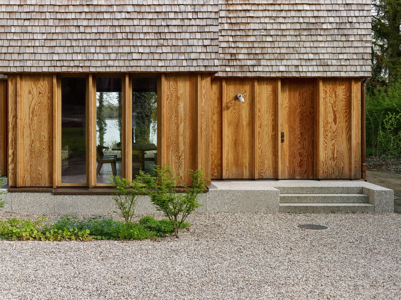 Architectural project - natural materials, wood, timber, sustainable design, warm tones, beige, brown, timber facade, exterior design, natural textures, organic design, tranquil setting, natural finish, warm wood, modern rustic, wood cladding, eco friendly home, timber house, stone, wood texture, cozy cabin, earthy tones, warm atmosphere, wooden architecture, nature-inspired, shingle roof, wooden facade, wooden panels, timber exterior, eco house, rustic home, countryside retreat, nature house, rural dwelling, gravel path, stone steps, simple entrance, minimalist exterior, country vibes, serene landscape, nature friendly, earthy facade, residential home, wooden retreat, timber siding, rustic aesthetic, forest home, wooden house