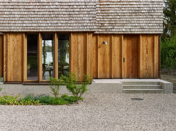 Architectural project - natural materials, wood, timber, sustainable design, warm tones, beige, brown, timber facade, exterior design, natural textures, organic design, tranquil setting, natural finish, warm wood, modern rustic, wood cladding, eco friendly home, timber house, stone, wood texture, cozy cabin, earthy tones, warm atmosphere, wooden architecture, nature-inspired, shingle roof, wooden facade, wooden panels, timber exterior, eco house, rustic home, countryside retreat, nature house, rural dwelling, gravel path, stone steps, simple entrance, minimalist exterior, country vibes, serene landscape, nature friendly, earthy facade, residential home, wooden retreat, timber siding, rustic aesthetic, forest home, wooden house