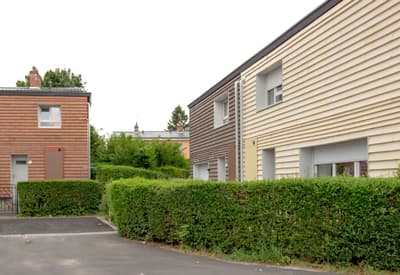 Architectural project - beige facade, exterior facade, cladding, horizontal lines, driveway, community living, row houses, townhouses, residential cluster, suburban housing, neat facade, brown facade, green hedges, manicured hedges, landscaped front, modern neighborhood, housing development, suburban style, compact houses, family homes, daylight capture, minimal design, natural materials, eco-friendly design, wood, timber, outdoor space, natural light, passive design, contemporary style, green, neutral tones, beige, brown, concrete, green architecture, modern facade, clean lines, white facade, timber cladding, wood cladding, white, energy efficient, brick, functional layout, modern living, residential area, simple architecture, linear facade, sustainable living, urban living
