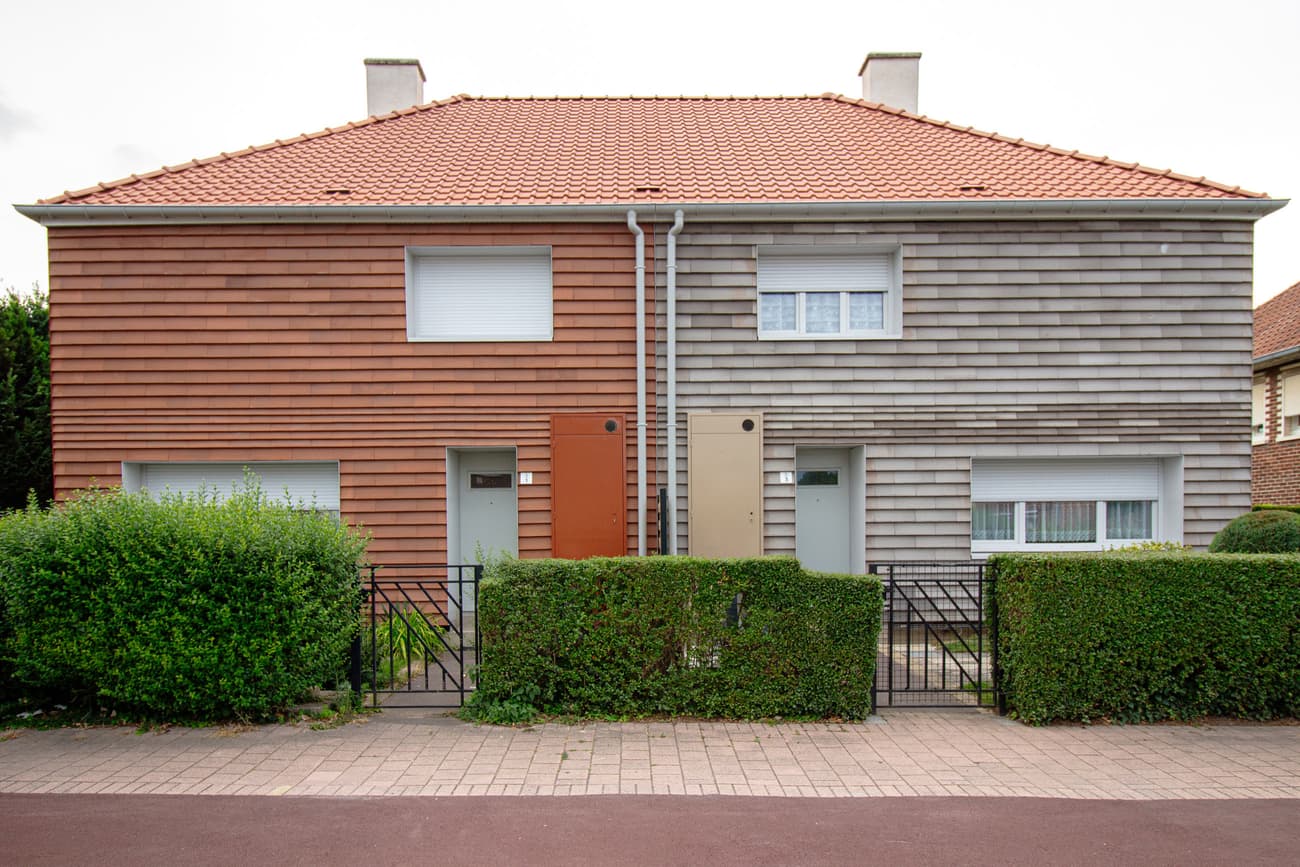 Architectural project - facade, duplex, side by side, stone cladding, gray, brickwork, symmetrical design, terracotta roof, two-tone facade, community living, lawn, pathway, privacy hedge, double doors, residential suburb, natural materials, sustainable materials, wood, warm tones, eco design, contemporary style, neutral tones, beige, brown, concrete, functional design, simple design, minimalist design, neutral colors, exterior, modern facade, clean lines, stone, clay, warm colors, terracotta, brick, brick facade, integrated design, wooden cladding, family home, residential building, light facade, green landscaping, modern suburb, architectural rhythm, energy efficiency, clay tiles, suburban house, urban living, urban housing, entryway