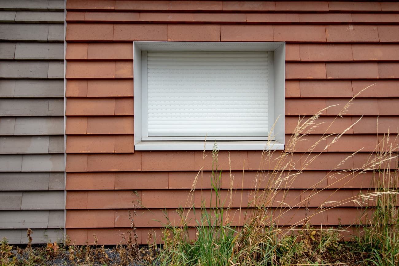 Architectural project - weathered look, residential exterior, tiled facade, red tiles, rural aesthetic, traditional vibe, earthen tones, terracotta facade, terracotta cladding, red cladding, white window, shuttered window, layered texture, minimalist window, simple window, natural materials, architectural detail, sustainable materials, warm tones, exterior design, exterior wall, functional design, farmhouse style, exterior detail, natural textures, durable materials, modern rustic, clean lines, white, textured wall, plaster, structural element, terracotta, rustic exterior, sustainable facade, contemporary facade, facade design, modern exterior, window detail, building envelope, eco facade, red