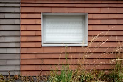 Architectural project - weathered look, residential exterior, tiled facade, red tiles, rural aesthetic, traditional vibe, earthen tones, terracotta facade, terracotta cladding, red cladding, white window, shuttered window, layered texture, minimalist window, simple window, natural materials, architectural detail, sustainable materials, warm tones, exterior design, exterior wall, functional design, farmhouse style, exterior detail, natural textures, durable materials, modern rustic, clean lines, white, textured wall, plaster, structural element, terracotta, rustic exterior, sustainable facade, contemporary facade, facade design, modern exterior, window detail, building envelope, eco facade, red