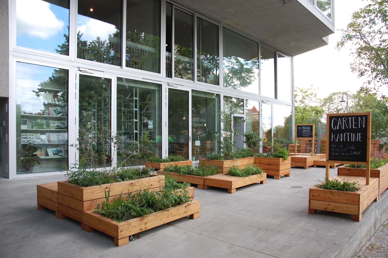 Architectural project - sustainability, terrace, concrete structure, sustainable space, natural elements, grey concrete, eco-friendly design, wood, timber, natural light, inviting atmosphere, outdoor living, glass, natural tones, eco design, grey, green, neutral tones, daylight, gathering space, concrete, light wood, urban oasis, contemporary design, casual setting, minimalist style, neutral colors, eco materials, outdoor cafe, social space, exterior, outdoor seating, biophilic design, modern facade, clean lines, indoor outdoor, modern architecture, open layout, dining area, alfresco dining, greenery, garden view, green design, seamless transition, urban garden, glass facade, versatile space