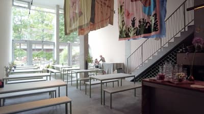 Architectural project - sleek railing, artistic vibe, bench seating, steel railing, modern cafe, metal details, art display, decorative art, natural materials, soft lighting, steel, relaxed vibe, natural light, sustainable design, pastel colors, glass, grey, green, neutral tones, daylight, concrete, industrial style, minimalist design, social space, gathering area, creative space, light tones, large windows, white, wood accents, garden view, grey floor, concrete floor, open space, airy atmosphere, greenery view, modern interior, glass wall, simple furniture, relaxing ambiance, high ceiling, double height, urban retreat