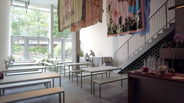 Architectural project - sleek railing, artistic vibe, bench seating, steel railing, modern cafe, metal details, art display, decorative art, natural materials, soft lighting, steel, relaxed vibe, natural light, sustainable design, pastel colors, glass, grey, green, neutral tones, daylight, concrete, industrial style, minimalist design, social space, gathering area, creative space, light tones, large windows, white, wood accents, garden view, grey floor, concrete floor, open space, airy atmosphere, greenery view, modern interior, glass wall, simple furniture, relaxing ambiance, high ceiling, double height, urban retreat