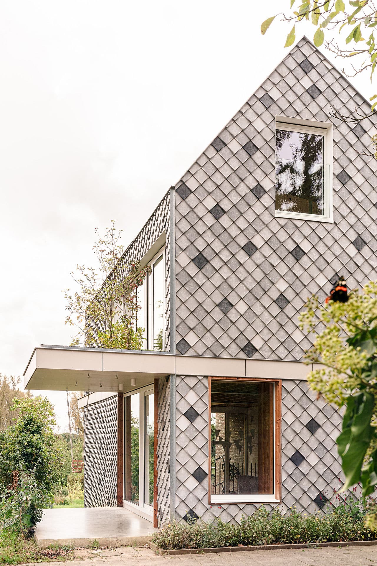 Architectural project - metal cladding, minimal architecture, elegant simplicity, lush landscape, modern roof, fresh vibe, overhang, natural materials, architectural detail, eco-friendly design, wood, timber, metal, outdoor space, natural light, glass, innovative design, grey, green, brown, roof design, exterior design, daylight optimization, neutral colors, geometric design, modern aesthetics, passive house, contemporary home, clean lines, large windows, earthy tones, textured finish, cozy atmosphere, natural environment, garden view, nature integration, sustainable house, inviting exterior, residential building, shingle facade, seamless transition, foliage, facade design, muted tones, modern house, architectural innovation