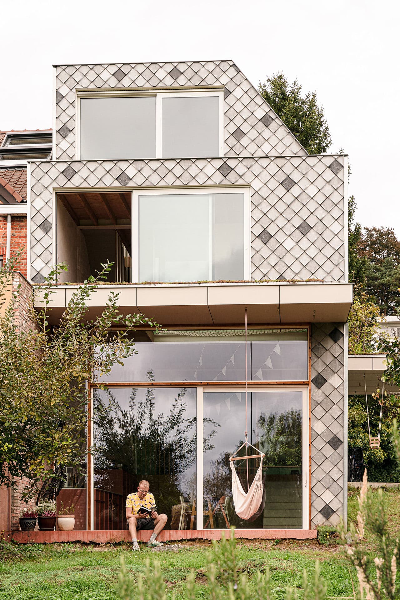 Architectural project - terrace, metal cladding, exterior tiles, patio, suburban living, double-height windows, grid pattern, tree-lined, geometric tiles, porch, wood, metal, natural light, outdoor living, passive design, glass, warm tones, eco design, contemporary architecture, grey, green, daylight, beige, exterior design, flat roof, serene atmosphere, Scandinavian style, neutral palette, glass doors, sustainable home, modern facade, large windows, energy efficient, residential design, tranquil vibe, relaxing space, Nordic vibe, garden view, cozy exterior, minimalist exterior, modern home, balcony design, sliding doors, natural surroundings, family-friendly, urban living
