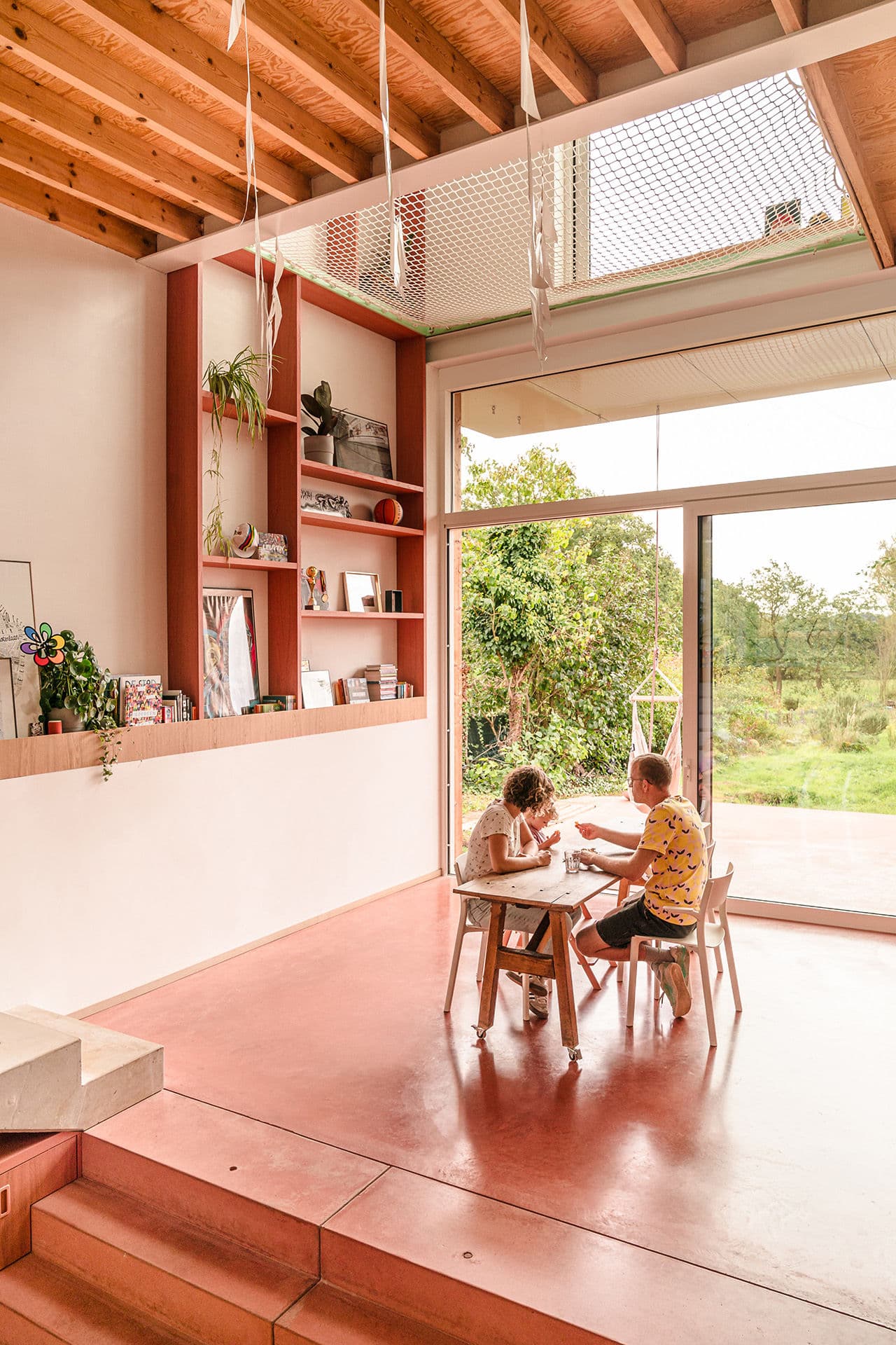 Architectural project - red floor, airy interior, red tones, minimal design, intimate space, natural materials, wood, timber, relaxed vibe, natural light, sustainable design, glass, warm tones, neutral tones, exposed beams, daylight, wooden ceiling, beige, multifunctional space, rustic modern, Scandinavian style, glass doors, vibrant space, earth tones, modern rustic, passive house, clean lines, indoor outdoor, white, eco friendly home, cozy vibe, inviting home, Nordic style, plaster, timber ceiling, open shelves, comfortable home, casual living, open layout, open plan, dining area, warm atmosphere, casual dining, terracotta, nature connection, garden view, textured walls, warm light, spacious interior, residential space, family home, bright space, sliding doors, plaster walls, greenery view, playful space, kid friendly, wooden shelves, terracotta floor, homey feel, family-friendly, living space, red