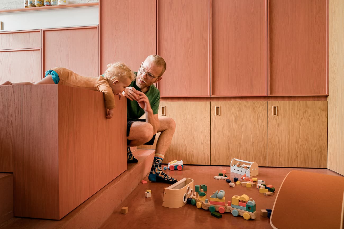 Architectural project - red floor, timber cabinets, family interaction, wooden toys, pastel, modular furniture, wood cabinets, pink, wood, timber, pastel colors, warm tones, functional design, contemporary design, Scandinavian style, minimalist design, cozy space, creative space, interactive design, Nordic design, family space, inviting space, warm atmosphere, terracotta, playful vibe, home interior, cozy home, playful space, playroom, children's room, kid friendly, learning environment, built-in storage, terracotta floor, home renovation, family-friendly, red