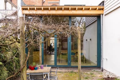 Architectural project - minimalist garden, green view, modern extension, patio, wooden pergola, backyard, residential extension, house extension, timber canopy, small patio, urban extension, outdoor table, outdoor chairs, maple wood, natural materials, timber, steel, outdoor space, natural light, glass, warm tones, contemporary style, green, daylight, beige, brown, light wood, multifunctional space, eco friendly, modern design, compact space, minimalist design, neutral colors, Scandinavian vibe, sustainable building, earth tones, stone, open plan, garden dining, cozy atmosphere, nature connection, bright interior, family home, sliding doors, urban garden, glass facade, indoor outdoor flow