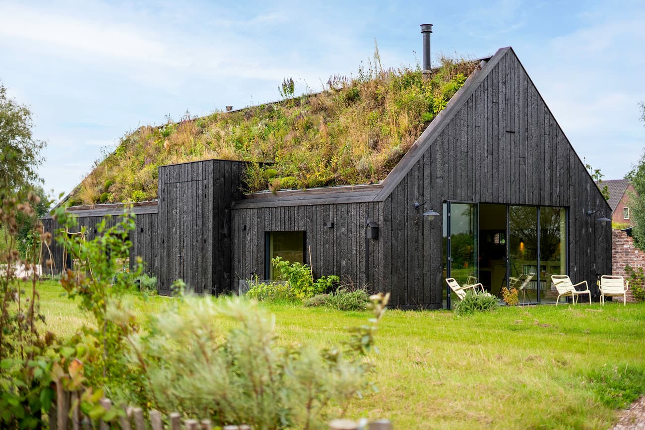 Architectural project - modern barn, sliding glass, garden chairs, garden setting, grass roof, black house, burnt wood, carbon neutral, serene vibe, wood, outdoor living, reclaimed materials, recycled materials, glass, eco design, sustainable architecture, green, wood facade, eco friendly, farmhouse style, rustic modern, rustic charm, Scandinavian style, minimalist design, black, outdoor seating, natural landscape, biophilic design, sustainable home, passive house, large windows, indoor outdoor, timber cladding, countryside home, energy efficient, nature-inspired, quiet retreat, secluded retreat, nature integration, green design, nordic influence, modern rural, natural insulation, environmentally conscious, green roof, living roof, low impact design, rural house, dark facade, charred timber