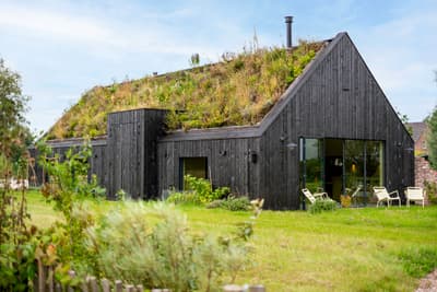Architectural project - modern barn, sliding glass, garden chairs, garden setting, grass roof, black house, burnt wood, carbon neutral, serene vibe, wood, outdoor living, reclaimed materials, recycled materials, glass, eco design, sustainable architecture, green, wood facade, eco friendly, farmhouse style, rustic modern, rustic charm, Scandinavian style, minimalist design, black, outdoor seating, natural landscape, biophilic design, sustainable home, passive house, large windows, indoor outdoor, timber cladding, countryside home, energy efficient, nature-inspired, quiet retreat, secluded retreat, nature integration, green design, nordic influence, modern rural, natural insulation, environmentally conscious, green roof, living roof, low impact design, rural house, dark facade, charred timber