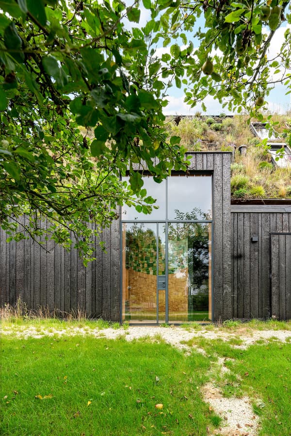 Architectural project - retreat home, garden house, calm environment, grass roof, burnt wood, full-height window, black finish, black facade, natural materials, wood, timber, outdoor space, natural light, passive design, green building, green, neutral tones, beige, exterior design, wood exterior, rustic charm, Scandinavian style, minimalist design, black, low carbon, biophilic design, eco home, contemporary home, landscape integration, large window, outdoor view, energy efficient, earthy tones, forest retreat, rural setting, nature house, sustainable house, modern home, nordic influence, vertical cladding, nature blend, green space, living roof, countryside setting, charred wood