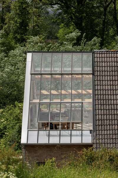 Architectural project - brickwork, transparent facade, grey tiles, roof tiles, brick foundation, window grids, framed glass, daylight design, lush setting, passive solar gain, harmonious blend, textured materials, atmospheric, forest environment, cream tones, terracotta tiles, functional aesthetic, minimal design, natural materials, architectural detail, natural light, warm tones, eco design, sustainable architecture, outdoor setting, exterior design, rural architecture, rustic modern, contemporary design, eco-friendly materials, modern rustic, biophilic design, scenic view, landscape integration, clean lines, light filled, indoor outdoor, modern architecture, countryside home, wood accents, earthy tones, pitched roof, nature-inspired, triangular roof, nature connection, brick base, garden view, cozy design, timber framing, seamless integration, green surroundings, simple lines, glass facade, energy efficiency, glass wall, clay tiles
