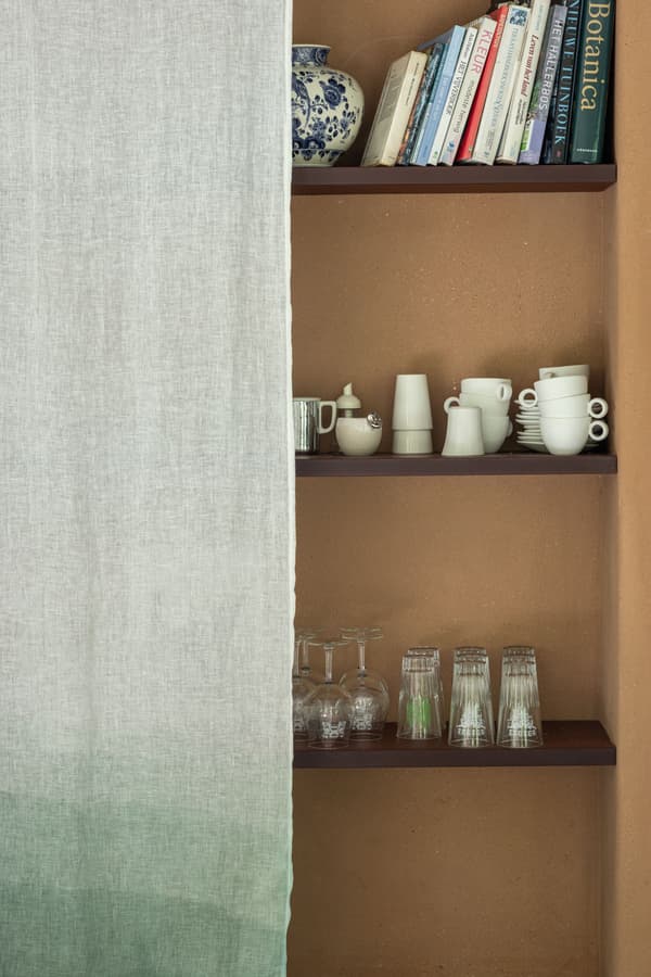 Architectural project - fabric curtain, green curtain, home shelving, kitchen shelving, ceramic cups, glassware, pottery, kitchen display, relaxed style, earthy style, brown wall, gradient curtain, natural materials, wood, timber, casual style, sustainable design, warm tones, natural tones, green, neutral tones, beige, brown, eco friendly, farmhouse style, rustic vibe, natural textures, cozy vibe, inviting home, Nordic style, textured wall, plaster wall, plaster, cozy kitchen, open shelves, kitchen storage, comfortable home, informal dining, dining area, terracotta wall, clay, rustic design, Mediterranean style, terracotta, warm vibe, beige wall, breakfast nook, simple decor, minimal decor, clay wall, wooden shelves, rustic kitchen