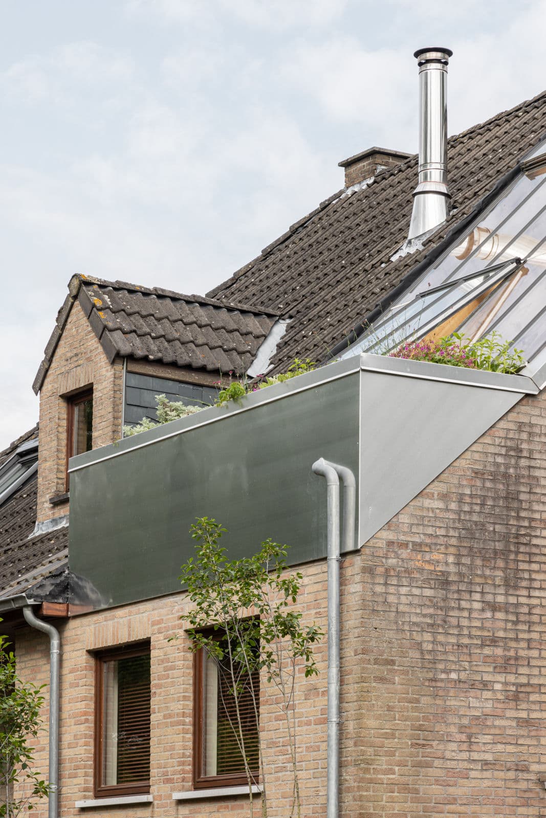 Architectural project - metal cladding, rooftop garden, traditional meets modern, exposed brick, home extension, modern extension, masonry facade, zinc cladding, contemporary addition, brick exterior, rainwater pipes, guttering, integrated planting, urban ecology, energy-efficient home, multi-material facade, European villa, cladding contrast, garden integration, suburban living, modern roofline, zinc, rambler style, facade diversity, natural materials, metal, warm tones, modular design, eco design, sustainable architecture, passive house, natural ventilation, stone, compact design, chimney, earthy tones, sloped roof, pitched roof, brick, brick facade, exterior view, nature integration, residential home, residential building, green roof, mixed materials, suburban house, urban gardening