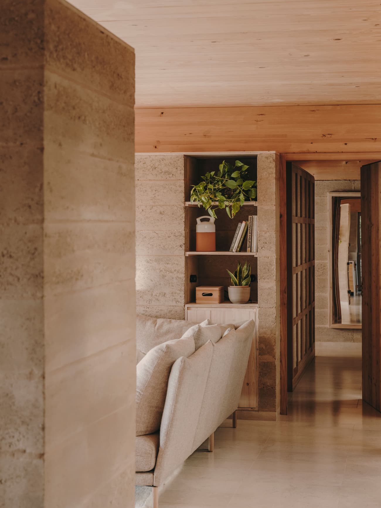 Architectural project - casual vibe, living room, muted colors, plant decor, earth wall, terracotta walls, integrated shelves, informal space, warm interior, natural materials, sustainable materials, natural light, warm tones, eco design, neutral tones, beige, light wood, modern aesthetic, eco friendly, timber beams, rustic modern, minimalist style, soft textures, rammed earth, earth tones, modern rustic, earth-friendly, sustainable home, relaxed living, inviting space, relaxing space, greenery, comfortable seating, calm atmosphere, earthy textures, wood ceiling, cozy home, interior design, open shelving, seamless design, home living