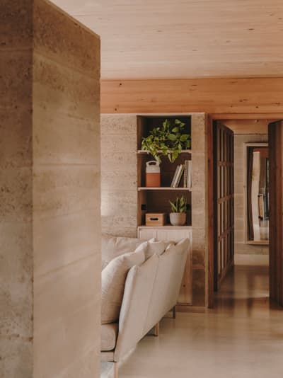 Architectural project - casual vibe, living room, muted colors, plant decor, earth wall, terracotta walls, integrated shelves, informal space, warm interior, natural materials, sustainable materials, natural light, warm tones, eco design, neutral tones, beige, light wood, modern aesthetic, eco friendly, timber beams, rustic modern, minimalist style, soft textures, rammed earth, earth tones, modern rustic, earth-friendly, sustainable home, relaxed living, inviting space, relaxing space, greenery, comfortable seating, calm atmosphere, earthy textures, wood ceiling, cozy home, interior design, open shelving, seamless design, home living