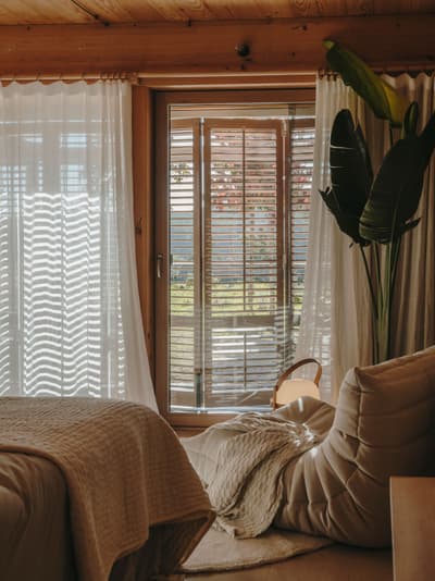 Architectural project - warm bedroom, hygge, bedroom, sheer curtains, natural bedroom, armchair, layered textiles, retreat vibe, natural materials, eco-friendly design, wood, timber, fabric, timber frame, natural light, bohemian style, warm tones, neutral tones, beige, light wood, Scandinavian influence, rustic modern, serene space, soft textures, modern rustic, biophilic design, sustainable home, white, window view, inviting home, Nordic style, wood frame, beige tones, cozy nook, timber ceiling, earthy feel, relaxing space, cozy corner, garden view, lounge chair, comfortable living, wood ceiling, minimal decor, peaceful atmosphere, cozy bedroom, warm palette, indoor plant, organic textures, tranquility, living space
