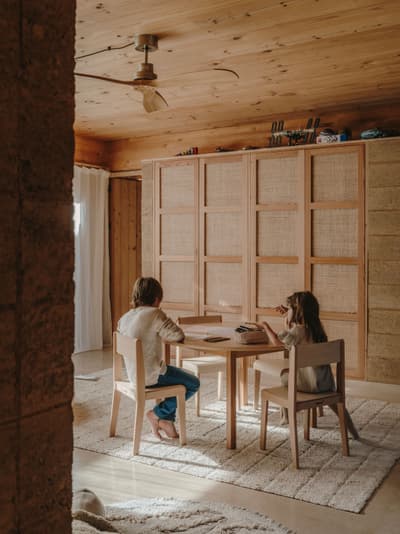 Architectural project - cozy living, home decor, minimalist furniture, calm environment, ceiling fan, small space living, woven details, kids area, floor rug, plush rug, textured fabric, natural materials, wood, timber, raw materials, natural light, warm tones, eco design, neutral tones, daylight, wooden ceiling, beige, brown, light wood, multifunctional space, honey wood, rustic modern, intimate setting, Scandinavian style, relaxed atmosphere, timber panels, modern rustic, sustainable home, Nordic design, cozy vibe, inviting home, casual living, timber interior, family space, living area, wooden table, textured walls, warm vibe, seating area, wood ceiling, interior design, simple furniture, home study, wood interior
