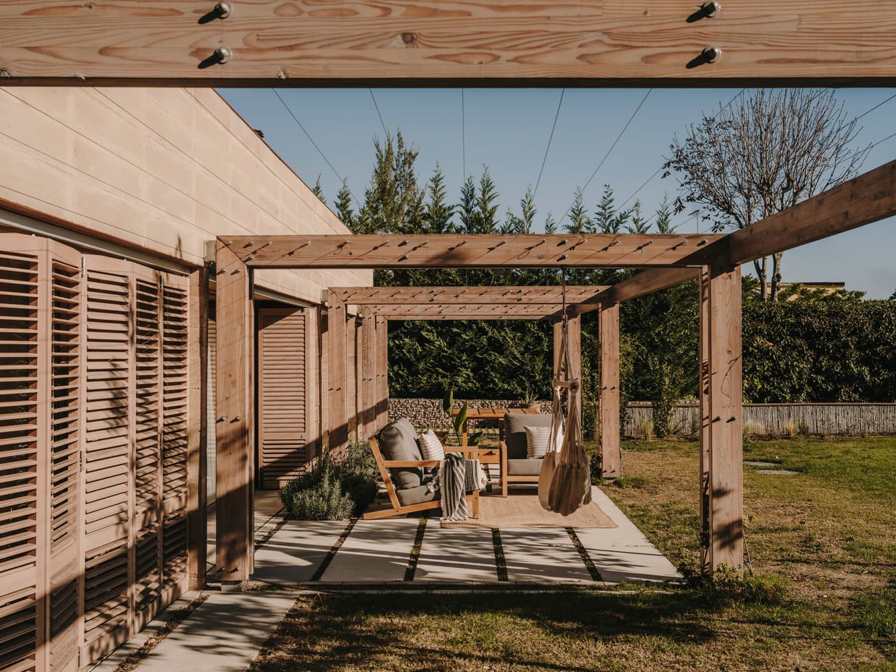 Architectural project - wooden shutters, outdoor lounge, wooden pergola, timber pergola, garden terrace, patio seating, outdoor furniture, al fresco, garden decor, landscaped garden, sustainable materials, wood, timber, relaxed vibe, natural light, outdoor living, warm tones, eco design, outdoor area, neutral tones, beige, natural setting, timber construction, rustic modern, wood structure, timber walls, modern rustic, earthy tones, warm atmosphere, cozy outdoor, garden design, relaxing space, garden retreat, landscape design, sunny day, backyard retreat, garden view, nature integration, outdoor shelter, open air, lounge chairs, comfortable seating, inviting exterior, garden seating, residential garden, home garden, green space