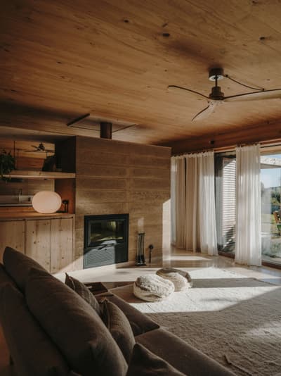 Architectural project - fireplace, sheer curtains, cozy living space, relaxing lounge, stone fireplace, floor cushions, plush cushions, soft rug, warm interior, serene environment, wood, timber, natural light, passive design, daylight, beige, brown, light wood, eco friendly, natural textures, Scandinavian style, neutral palette, tranquil setting, timber walls, exposed wood, earth tones, modern rustic, biophilic design, sustainable home, large windows, indoor outdoor, Nordic design, stone, wood walls, timber ceiling, comfortable home, open layout, living area, inviting space, minimalist decor, nature-inspired, residential design, calm atmosphere, wood ceiling, rustic living room, natural finishes, earthy vibes