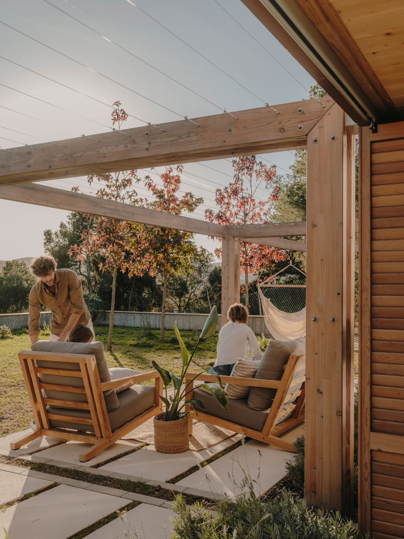 Architectural project - backyard lounge, cozy patio, modern patio, wooden pergola, timber pergola, garden chairs, hammock, garden pergola, timber posts, peaceful garden, residential outdoor, open air space, garden relaxation, garden furniture, leisure area, wood, timber, outdoor space, warm sunlight, natural light, outdoor living, sustainable design, natural tones, beige, brown, natural setting, retreat space, serene atmosphere, casual seating, relaxation spot, outdoor seating, earthy tones, eco friendly space, landscape design, lounge chairs, wooden structure, private garden, patio furniture, green space, laid-back vibe, family area