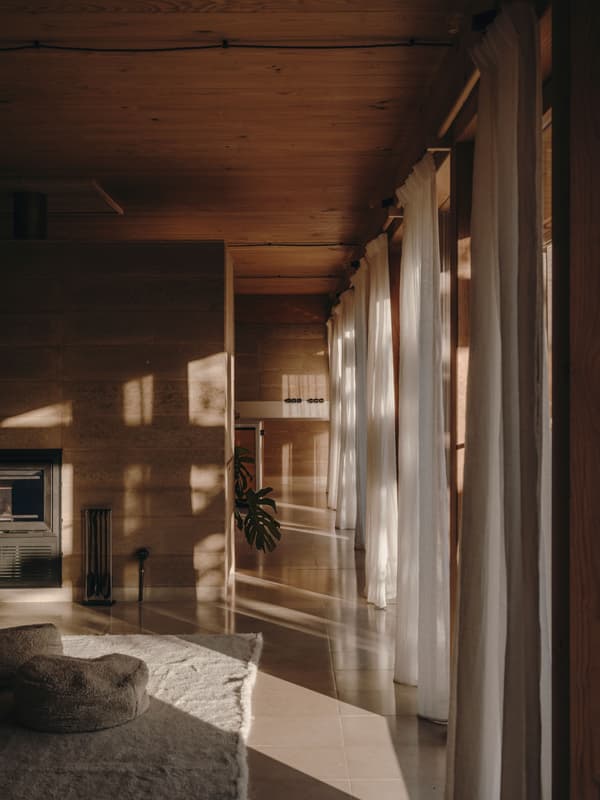 Architectural project - rustic elegance, living room, plant decor, rammed earth walls, floor-to-ceiling curtains, sheer curtains, natural flooring, relaxation space, cozy interior, warm interior, natural materials, tranquil space, relaxed vibe, natural light, sustainable design, warm tones, wooden ceiling, beige, brown, light wood, eco friendly, honey wood, natural textures, architectural lighting, Scandinavian style, neutral palette, minimalist design, soft textures, timber walls, modern rustic, passive house, clean lines, large windows, energy efficient, wood walls, comfortable home, inviting space, earthy tones, simple living, textured walls, warm light, stone flooring, lounge area, nordic influence, wood ceiling, airy atmosphere, Japandi style, indoor plants