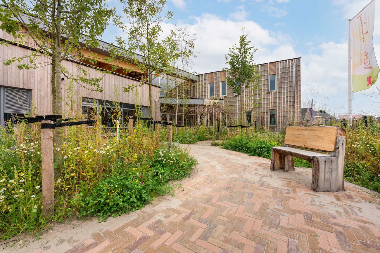 Architectural project - native plants, wild garden, garden, nature integrated, garden bench, path, brick path, herringbone path, landscaped grounds, wooden bench, wood, timber, passive design, modular design, eco design, community space, outdoor area, sustainable architecture, green, neutral tones, daylight, beige, wood facade, timber facade, natural textures, exterior, public space, outdoor seating, tranquil setting, natural building, biophilic design, inviting space, earthy tones, garden design, brick, environmentally friendly, cozy exterior, wooden cladding, rustic exterior, courtyard, urban green, contemporary building, outdoor vibes