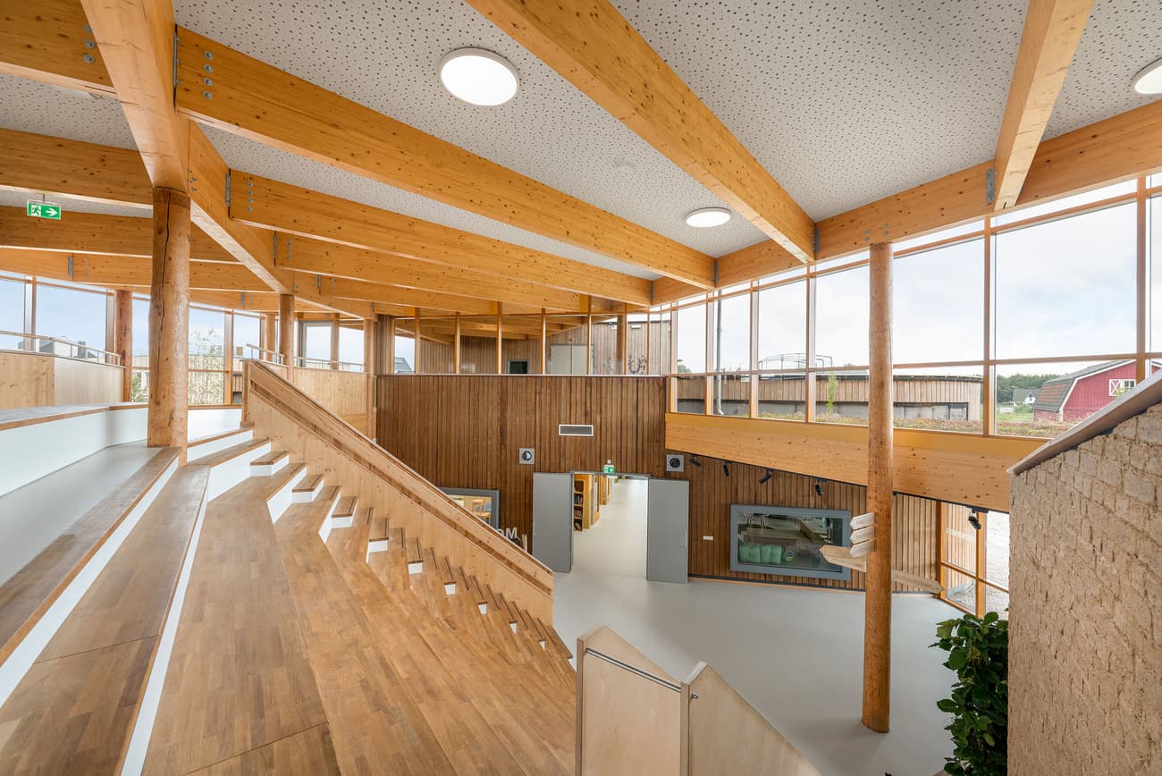 Architectural project - spacious design, amphitheater, stepped seating, acoustic design, structural elegance, modern venue, warm interior, indoor space, wood, timber, natural light, inviting atmosphere, passive design, sustainable design, contemporary style, neutral tones, exposed beams, timber structure, daylight, plywood, gathering space, beige, brown, light wood, engineered wood, multifunctional space, eco friendly, honey wood, wood beams, Scandinavian style, social space, community hub, community center, eco building, wood structure, circular design, natural ventilation, light filled, timber cladding, wood cladding, white, modern architecture, Nordic style, timber ceiling, open plan, green design, bright interior, open space, educational space, public building, welcoming space, wooden walls