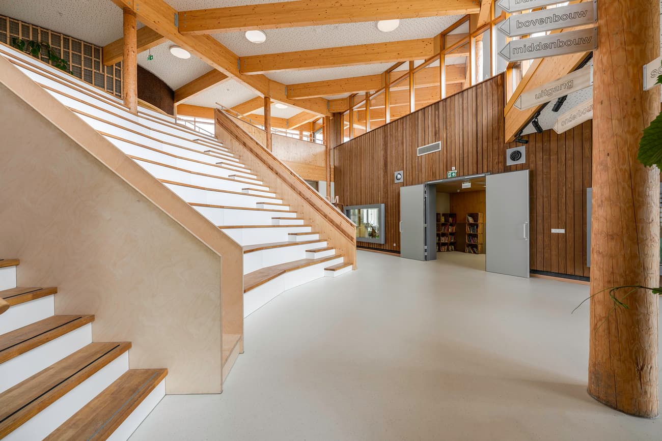 Architectural project - public access, airy interior, skylights, open stair, lobby, wide stairs, wooden rails, library entrance, education space, educational environment, fresh vibe, natural materials, raw materials, natural light, passive design, sustainable design, eco design, sustainable construction, contemporary style, exposed beams, beige, light wood, daylight optimization, honey wood, timber beams, minimalist design, neutral colors, community center, eco-friendly materials, timber walls, circular construction, large windows, wood cladding, modern architecture, Nordic style, wood walls, timber interior, inviting space, warm atmosphere, wooden flooring, timber flooring, spacious interior, Scandinavian design, bright space, structural elements, public building, glass facade, learning center, modern interior, natural finishes, wooden columns, atrium, high ceiling, wood interior