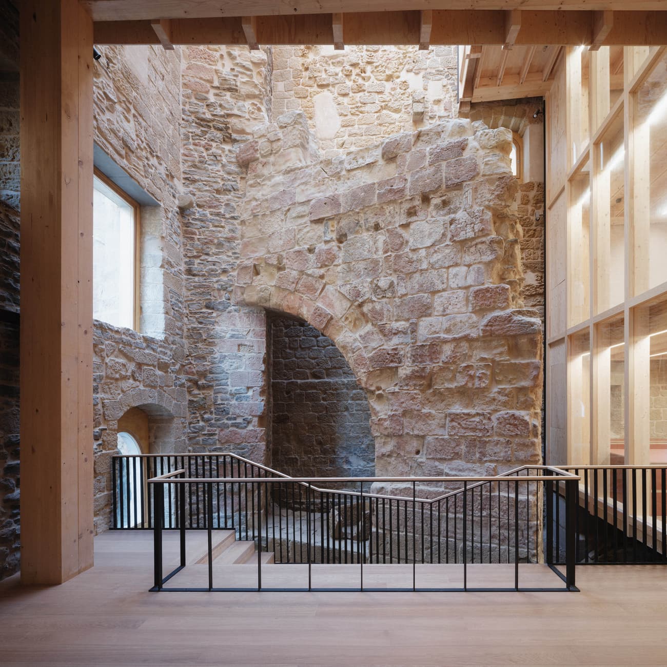 Architectural project - metal railing, exposed stone, cozy ambiance, rustic elegance, harmonious blend, glass enclosure, historic preservation, structural contrast, architectural heritage, black metal, historic renovation, wood, timber, metal, timber frame, natural light, inviting atmosphere, glass, warm tones, timber structure, daylight, beige, brown, light wood, honey wood, wood beams, rustic charm, neutral palette, black, adaptive reuse, wood floor, light filled, earthy materials, stone, airy space, open plan, stone wall, heritage building, timeless design, architectural contrast, double height, stone texture
