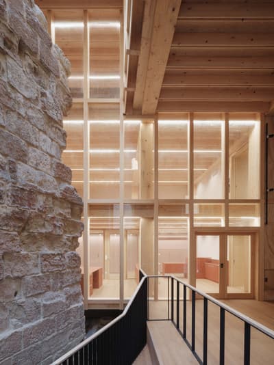 Architectural project - open ceiling, landmark building, historic meets modern, modern venue, minimal design, cozy interior, warm interior, natural materials, wood, timber, raw materials, natural light, sustainable design, glass, warm tones, eco design, neutral tones, timber structure, exposed beams, daylight, gathering space, beige, brown, light wood, natural wood, golden, modern design, timber construction, simple design, honey wood, timber beams, social space, public space, event space, timber panels, wood panels, Nordic design, textured wall, stone, timber interior, inviting space, stone wall, rustic wall, warm light, green design, Scandinavian design, bright interior, architectural contrast, contemporary space, glass wall, structural rhythm, wood interior