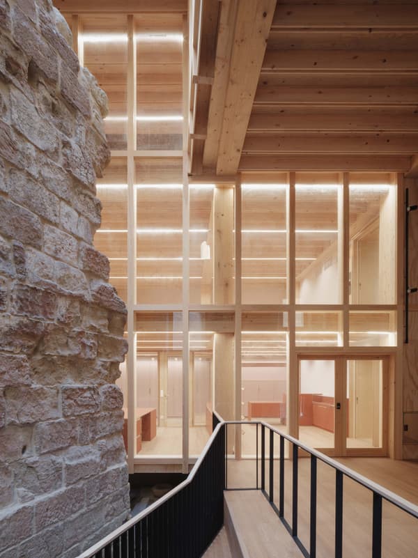 Architectural project - open ceiling, landmark building, historic meets modern, modern venue, minimal design, cozy interior, warm interior, natural materials, wood, timber, raw materials, natural light, sustainable design, glass, warm tones, eco design, neutral tones, timber structure, exposed beams, daylight, gathering space, beige, brown, light wood, natural wood, golden, modern design, timber construction, simple design, honey wood, timber beams, social space, public space, event space, timber panels, wood panels, Nordic design, textured wall, stone, timber interior, inviting space, stone wall, rustic wall, warm light, green design, Scandinavian design, bright interior, architectural contrast, contemporary space, glass wall, structural rhythm, wood interior