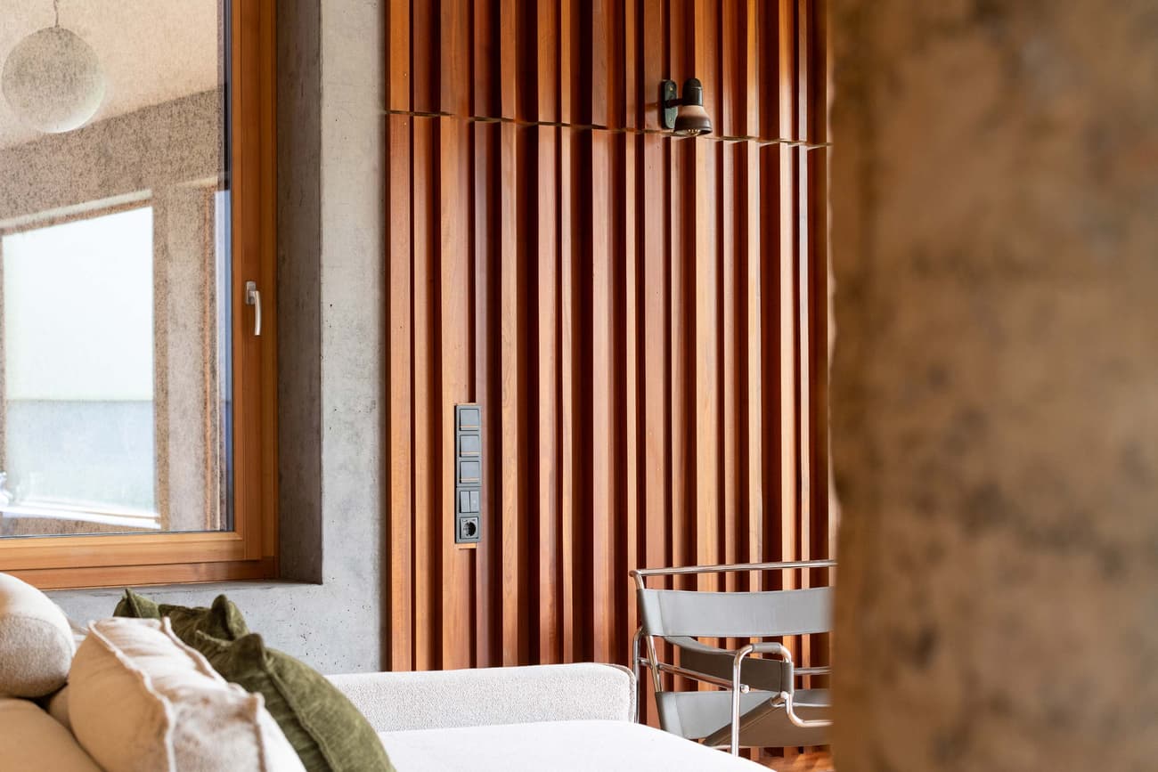 Architectural project - exposed concrete, feature wall, accent wall, natural elements, relaxing vibe, timber slats, concrete column, interior decor, cozy interior, natural materials, wood, timber, natural light, sustainable design, warm tones, daylight, beige, concrete, light wood, eco friendly, contemporary design, industrial touch, Scandinavian style, neutral palette, casual seating, soft textures, biophilic design, passive house, Nordic style, textured wall, green home, wood slats, comfortable seating, minimalist aesthetic, modern furniture, calm atmosphere, lounge area, modern living, vertical slats, home improvement, modern interior, residential interior, living space, urban retreat