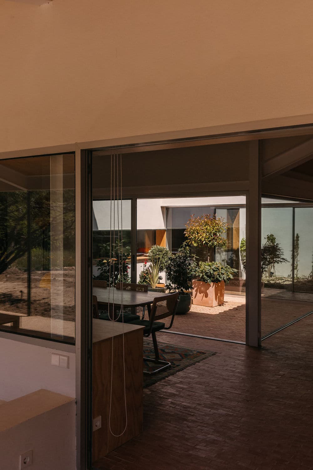 Architectural project - terrace, lush plants, potted plants, elegant simplicity, patio, brick flooring, zen garden, serene vibe, tranquil space, timber, natural light, passive design, sustainable design, warm tones, green, neutral tones, beige, brown, concrete, light wood, eco friendly, airy design, private retreat, minimalist design, relaxed atmosphere, exterior, outdoor seating, eco construction, indoor outdoor, modern architecture, earthy materials, wood accents, casual living, glass walls, inviting space, green home, earthy tones, greenery, garden view, modern home, contemporary house, sliding doors, soft tones, residential, open space, architectural elegance, courtyard, terracotta floor, brick texture